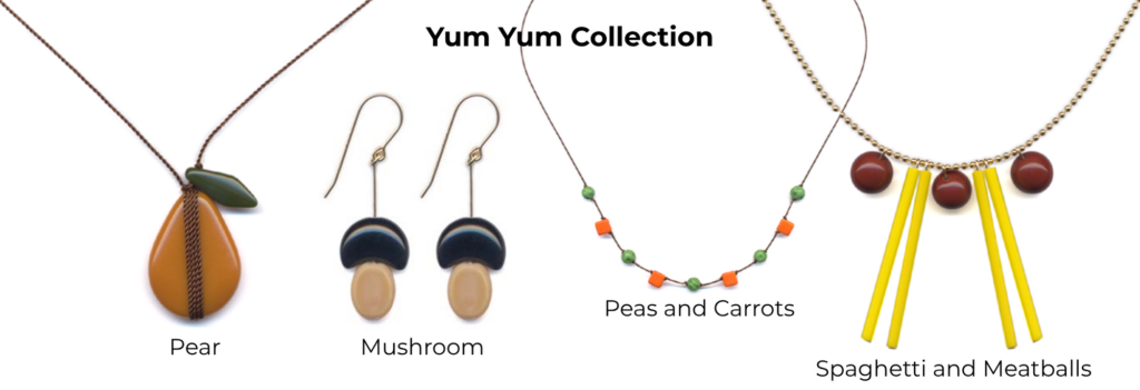 A sample of jewelry pieces from I. Ronni Kappos’ “Yum Yum Collection” which was inspired by foods of all kinds. Shown are “Pear” necklace featuring a pear shaped warm tan colored bead accented by a darker green leaf-shaped bead on top, a pair of “Mushroom” earrings each with 2 beads, one tan oval as the stem and a curved half-moon shaped dark brown bead as the cap, a “Peas and Carrots” necklace which is made of alternating textured round pea-green beads and square bright orange beads mimicking the look of frozen peas and carrots and the “Spaghetti and Meatballs” necklace with 3 spherical brown beads with twin long yellow vertical beads placed between the brown “meatball” beads.